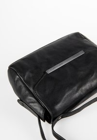 Zwarte leren schoudertas met een gladde textuur, rechthoekige vorm en een subtiele metalen accent aan de voorkant, voorzien van een schouderriem.