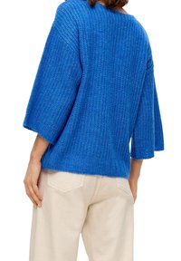 Pullover azzurro lavorato a maglia con una finitura testurizzata, caratterizzato da maniche ampie e una vestibilità morbida, abbinato a pantaloni chiari.