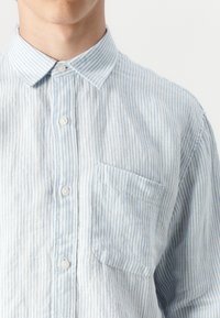 Light blue striped button-up shirt made of fabric with a textured finish, featuring a chest pocket and standard collar design.
