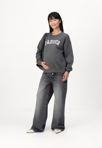 Sudadera gris con el texto "DAKOTA", combinada con jeans de pierna ancha en gris deslavado. Zapatos de punta clara. Texturas simples y suaves.