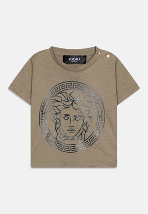 Camiseta de algodón color caqui con un gráfico circular de Medusa en plata, con cuello redondo y detalles dorados cerca del hombro. Etiqueta de Versace visible.
