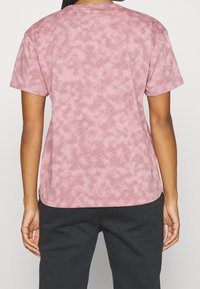 Růžové tričko s měkkým, texturovaným povrchem, krátkými rukávy a volným střihem. Obsahuje kulatý výstřih a mírně zakřivený lem.