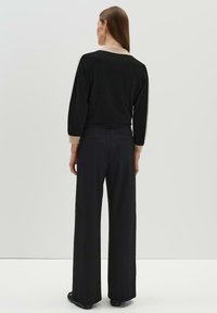 Black long-sleeve sweater with beige accents at cuffs and neckline, paired with high-waisted black wide-leg pants, displayed from the back.