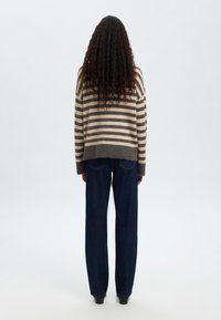 Gestreifter Strickpullover in Beige und Dunkelgrau, verkürztes Design, kombiniert mit dunkelblauen weiten Jeans. Weiche Textur, lockere Passform.