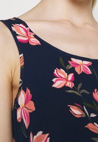 Laivastonsininen kukkakuosiset paita, jossa on vaaleanpunaisia ja valkoisia kukkia, pyöreä kaula-aukko ja hihaton malli, valmistettu pehmeästä ja sileästä kankaasta.