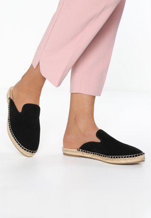 Zapatos negros de ante sin cordones con diseño recortado, ribete de yute y suela plana. Combinados con pantalones rosas a medida, acentuando la forma del zapato.