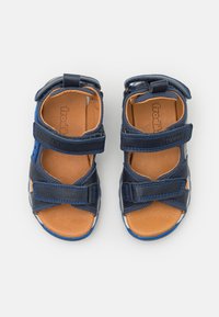 Blå lær sandaler med justerbare stropper, brune innersåler og lyse såler. Har kryssremdesign og ventilasjonshull.