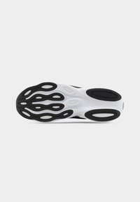 Suola di una scarpa da ginnastica bianca e nera con motivi di battistrada ovali e curvi neri su base bianca, su sfondo grigio uniforme.