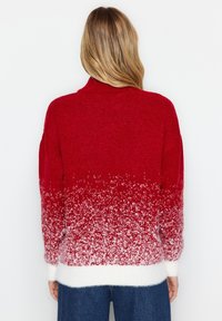 Punainen ja valkoinen gradienttisweater, jossa on pörröinen texture, korkea kaulus ja ribbituet hihnat. Muotoilu esittää ombre-efektiä kirkkaasta punaisesta valkoiseen.