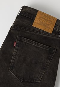 Πίσω τσέπη και δερμάτινη ετικέτα Levi Strauss & Co. σε σκούρο μαύρο τζιν με κόκκινη ετικέτα Levi's ορατή στην πλευρά της τσέπης.