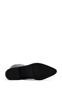 Bota de cuero negro con punta afilada y suela plana de goma. Costura interior visible a lo largo de los lados; acentos decorativos mínimos.