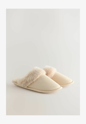 Chaussons beiges avec une bordure en fausse fourrure douce, un design à bout rond et un tissu texturé. La semelle est plate et flexible.