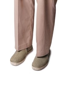 Espadrillas verdi in tela con suole in juta intrecciata, esibite con pantaloni beige, caratterizzate da una punta rotonda e dettagli cuciti lungo il bordo.