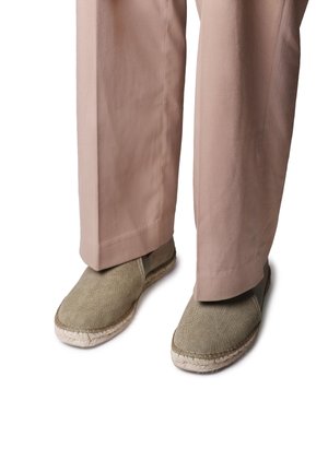 Espadrilles en toile verte avec des semelles en jute tressé, présentées avec un pantalon beige, comportant un bout arrondi et des détails cousus le long du bord.