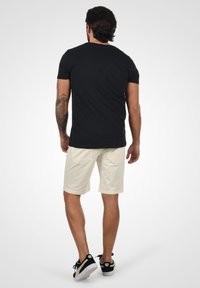 Svart kortermet T-skjorte kombinert med lysebeige shorts. Shortsene har to baklommer og en avslappet passform. Svarte sneakers fullfører looken.