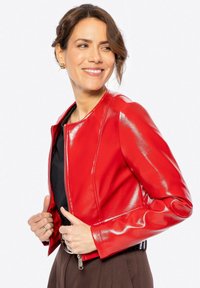 Veste courte en cuir verni rouge, avec un col rond et une fermeture éclair. Dispose de manches ajustées et d'une silhouette épurée.