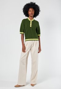 Green knitted polo sweater with short sleeves, yellow accents, and buttons. Paired with cream wide-leg trousers and beige pointed shoes.