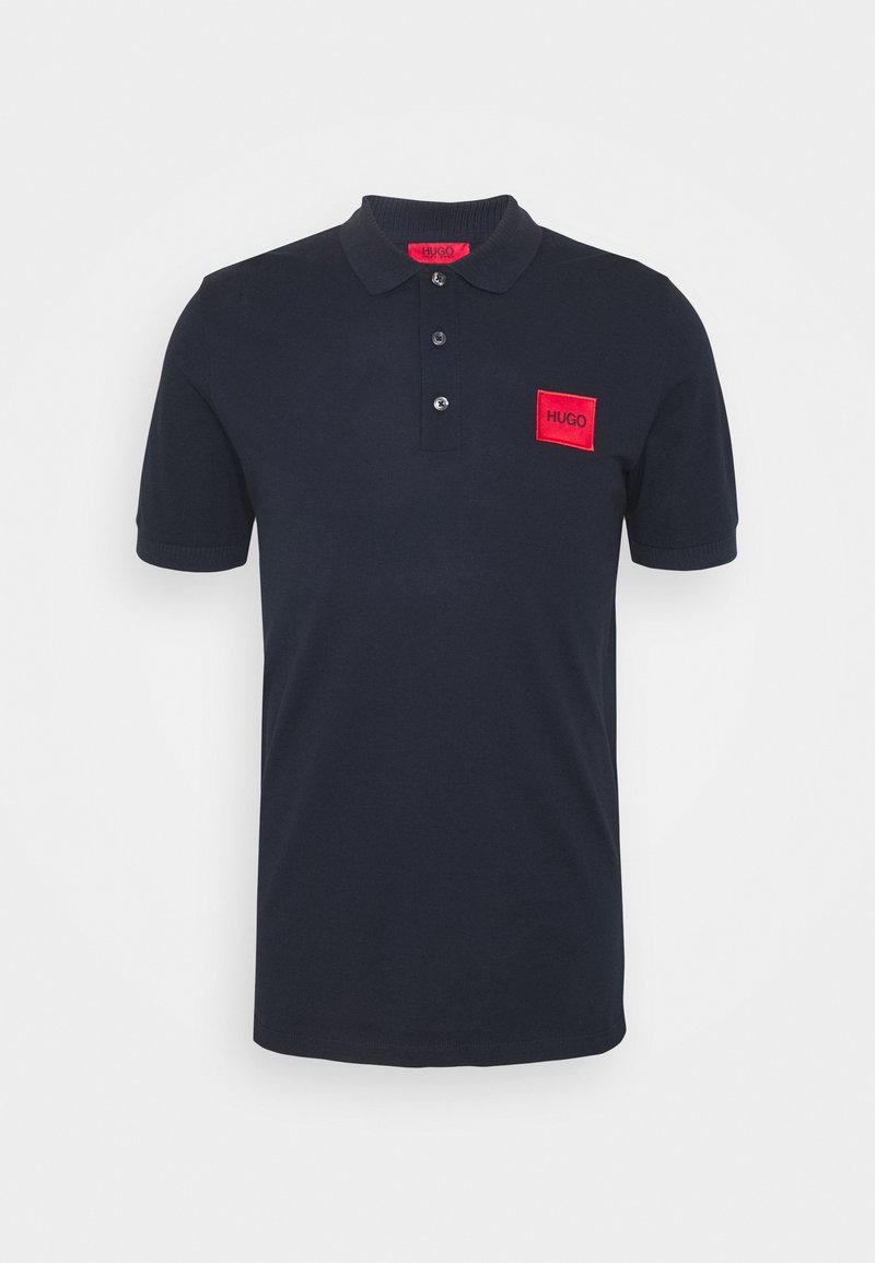 Polo-shirt bleu marine en coton, avec un col côtelé, une patte de boutonnage à trois boutons et un écusson rectangulaire rouge sur la poitrine gauche.
