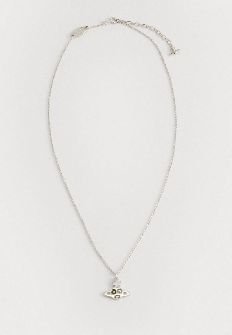 Colar de corrente de prata fina com um pequeno pendente em forma de crânio, apresentando detalhes de cruz e estrela sobre um fundo claro e liso.