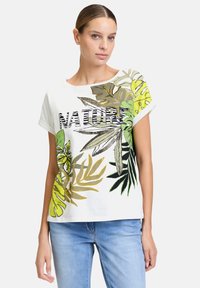 Biała koszulka z krótkim rękawem z zielonymi i żółtymi nadrukami liści. Napis "NATURE" z przodu w kolorze czarnym, o luźnym kroju i miękkiej fakturze.