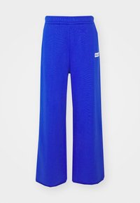 Siniset leveälahkeiset housut, jotka on valmistettu sileästä materiaalista, sisältävät elastisen vyötärön ja pienen valkoisen logon sivussa brändin tunnistamiseksi.