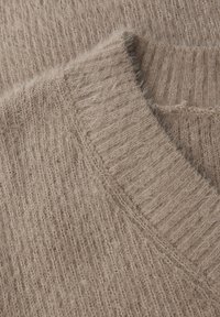 Beige gestrickter Pullover im Close-up, mit V-Ausschnitt, gerippter Textur und weichem, flauschigem Material mit einem dezenten Glanz.