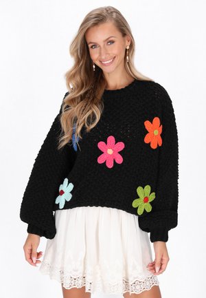 Schwarzer Strickpullover mit bunten Blumenapplikationen in Pink, Grün, Blau und Orange. Lockere Passform mit weiten Ärmeln und strukturiertem Stoff.