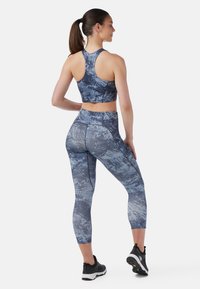 Sportbehå och leggins-set i ett blått abstrakt mönster, tillverkat av elastiskt material. Behån har en racerback-design; legginsen är caprilängd.