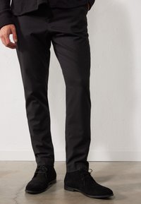 Pantaloni negri, croiți pe corp, dintr-o țesătură fină, asortați cu cizme negre din suede, cu sistem de închidere cu șireturi și tălpi plate.