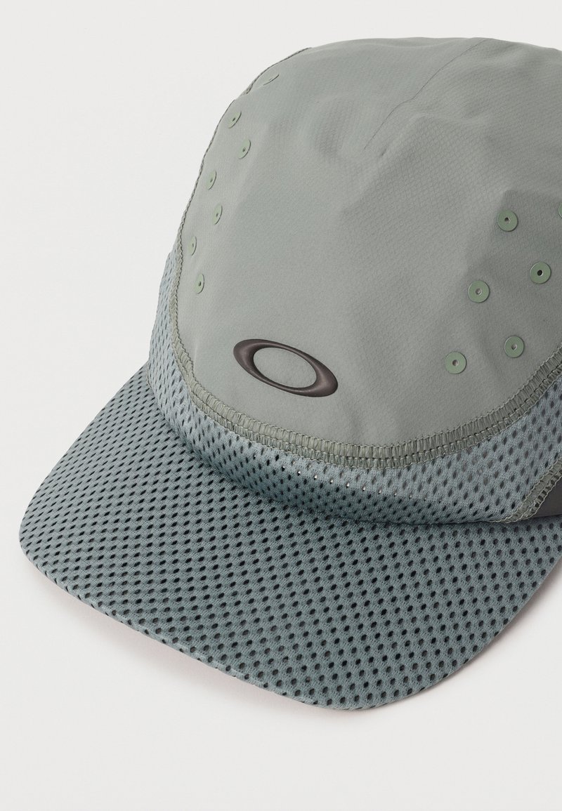 Lichtgrijze sportieve pet met geperforeerde mesh klep en ventilatiegaten, voorzien van een klein ovaal logo op het voorpaneel.