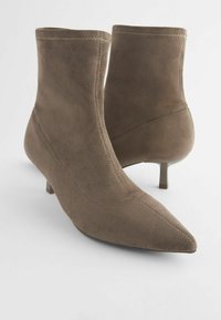Paire de bottines en daim taupe avec bouts pointus et petits talons kitten, présentées sur fond blanc.