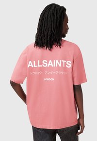 Rózsaszín, oversized póló fehér nyomtatott "ALLSAINTS" szöveggel és japán írással a hátsó részen. Sima pamut anyag, rövid ujjú, laza szabású.