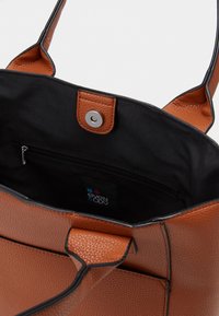 Bruine gestructureerde leren draagtas met twee handvatten, drukknoopsluiting en een zwart binnenvak. Voorzien van een merklabel aan de binnenkant.