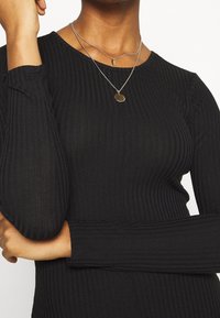 Svart ribbad långärmad topp med åtsittande design och rund halsringning. Lagda silverhalsband med en berlock framhäver halsringningen.