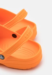 Sandalias de estilo Crocs en color naranja con dos tiras elevadas, plantilla texturizada y agujeros de drenaje circulares. Fabricadas con material ligero y flexible.