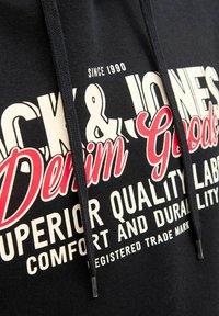 Sudadera negra con texto en negrita en blanco y rojo: "Jack & Jones Denim Goods", con cordones y una textura suave. Tejido duradero.