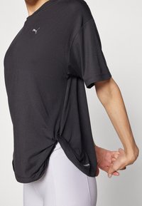 Svart atletisk t-shirt med ledig passform, rund halsringning och korta ärmar. Har en knutdetalj på sidan och en logga på bröstet.