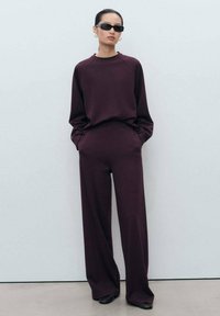 Burgundský dvojdielny outfit pozostávajúci z topu s dlhým rukávom a raglánovými rukávmi a širokými nohavicami, oboje z hladkej, textúrovanej látky.