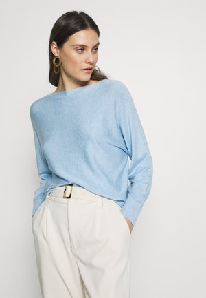 Pull à col bateau en maille bleu clair avec une coupe décontractée. Associé à un pantalon taille haute beige, orné d'une ceinture avec des accents noirs et dorés.