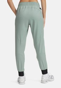 Light green tapered joggers with elastic waistband and black cuffs. Smooth texture, fitted design, and subtle seam detailing. White sneakers visible.