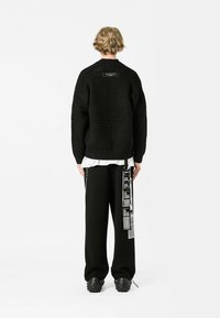 Jersey negro de punto con un patrón texturizado, corte oversize y una etiqueta en la parte posterior. Combinado con pantalones negros con acentos gráficos.