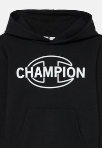 Melna kapuce ar priekšējo kabatu, kurā ir liels balts "CHAMPION" logo ovālas formas dizainā. Izgatavota no mīksta kokvilnas maisījuma auduma.