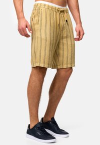 Shorts rayés beiges en tissu doux avec taille à cordon et poches latérales, portés avec des baskets bleu foncé.