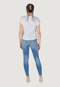 T-shirt bianco a maniche corte e jeans skinny azzurri chiari. I jeans sono scoloriti e dalla texture morbida, abbinati a tacchi nudi.