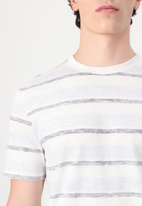 Hvit kortermet t-skjorte med tynne grå-blå horisontale striper, rund hals og myk, teksturert stoff.