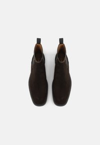 Bottes Chelsea en daim marron avec des empiècements élastiques, des languettes de tirage, un bout arrondi et une doublure intérieure lisse. Semelles en caoutchouc plates pour la stabilité.