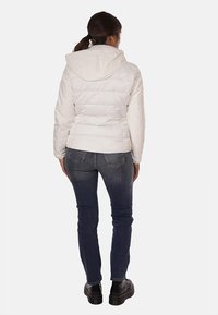 Giacca bianca imbottita con cappuccio, caratterizzata da cuciture orizzontali e una silhouette aderente, abbinata a jeans scuri e scarpe nere.