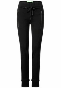 Svarta joggingsbyxor i texturerat tyg, elastisk midja, justerbar dragsko och fickor med dragkedja på sidorna. Åtsittande ankle-fållar.