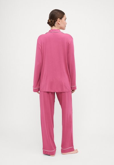 Ružový pyžamový komplet v uvoľnenom strihu, zahŕňajúci dlhé rukávy a nohavice. Materiál je hladký s bielymi lemami na manžetách a golieri.