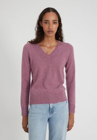 Helllila V-Ausschnitt Pullover aus weichem Material mit langen Ärmeln und geripptem Saum. Kombiniert mit hellblauen, geraden Jeans.